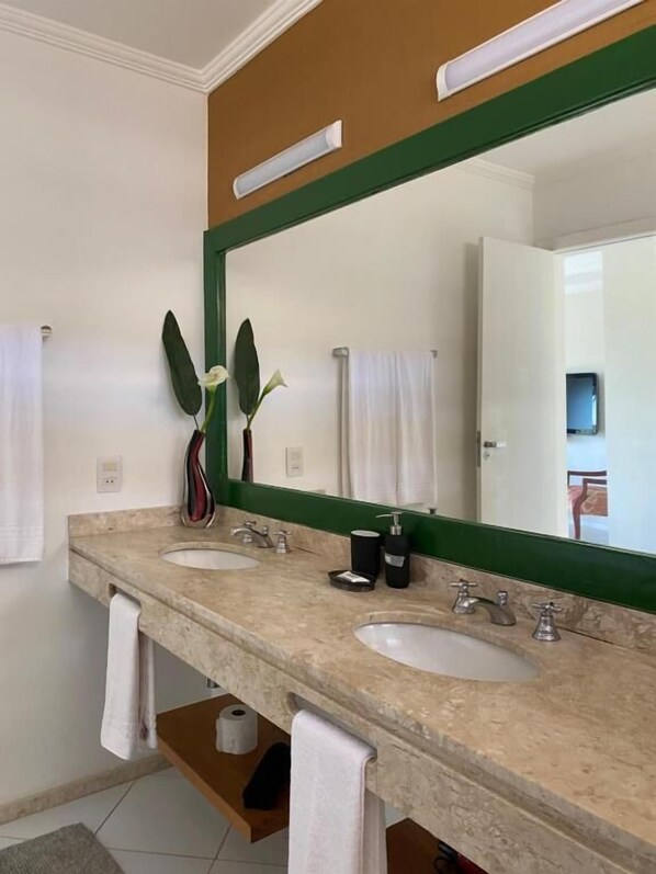 A bathroom with two sinks, a large mirror, and a green-framed mirror. There are towels hanging on the wall and a plant in the mirror. - Top De Buzios Boutique Hotel & Spa (Búzios)