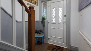 A hallway with a white door, a blue table with a plant, and a wooden staircase. - Stylish 3BR House | Perfect for Contrators & Extended Stays (Sheffield)