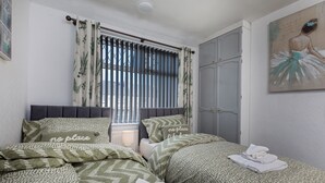 A bedroom with two beds, a window with curtains, a door, and a painting on the wall. - Stylish 3BR House | Perfect for Contrators & Extended Stays (Sheffield)