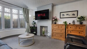 A living room with a fireplace, a television mounted on the wall, a sofa, a coffee table, and a wooden cabinet. - Stylish 3BR House | Perfect for Contrators & Extended Stays (Sheffield)