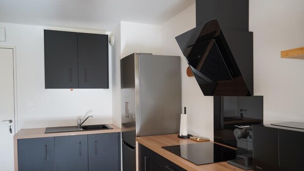 A modern kitchen with dark cabinetry, a stainless steel refrigerator, a built-in oven, and a coffee machine. - Quiet, warm apartment (Miniac-Morvan)