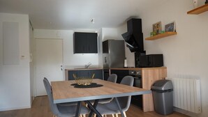 A modern kitchen with a dining table, chairs, and a trash bin. - Quiet, warm apartment (Miniac-Morvan)