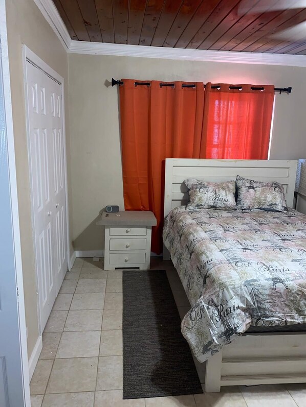 A bedroom with a bed, a nightstand, a door, and an orange curtain.