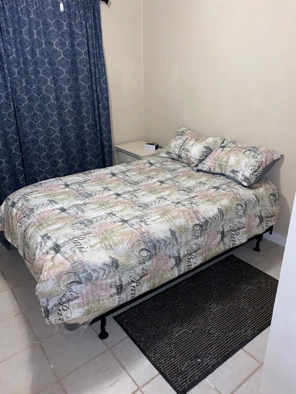 A bedroom with a bed, a nightstand, a black rug, and a curtain.