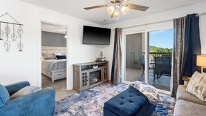A spacious living room with a fireplace, a ceiling fan, a television, and a large sliding glass door leading to an outdoor area. - Beautiful brand new sister condo's, no steps, located next to Silver Dollar City (Branson)