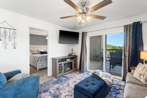 Ein geräumiges Wohnzimmer mit Kamin, Deckenventilator, Fernseher und einer großen Schiebetür zu einem Außenbereich.