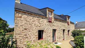 A stone building with a sloped roof, multiple windows with red frames, and a small front porch.