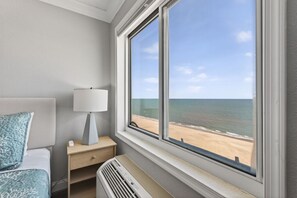 Ett hotellrum med en säng, ett nattduksbord med en lampa, en värmare och ett fönster med utsikt över stranden.