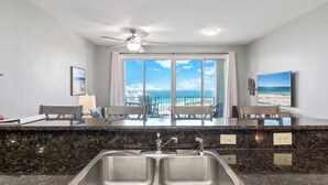 A modern kitchen with a large window, a ceiling fan, and a view of the beach.