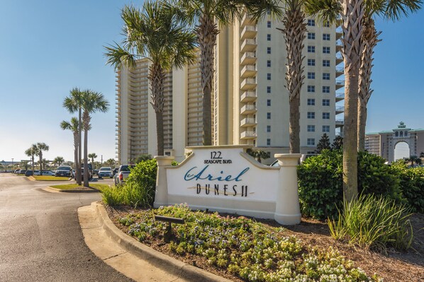 A sign for 'Ariel Dunes II' with a view of tall buildings and palm trees.