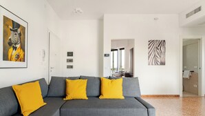 Een moderne woonkamer met een grijze bank en gele kussens, een schilderij met een zebra thema en een kunstwerk aan de muur met een zebra patroon.