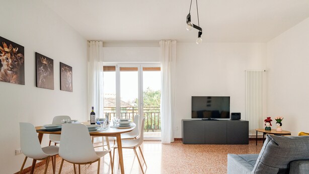 Een moderne woonkamer met een grijze bank, een eettafel met stoelen, een televisie op een kast en kunst aan de muur.