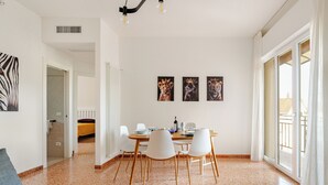 Een ruime woonkamer met een eettafel voor vier personen, een bank en een groot raam met gordijnen.