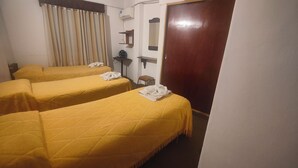Een hotelkamer met twee enkele bedden, een houten deur, een tafeltje met een ventilator en een spiegel aan de muur.