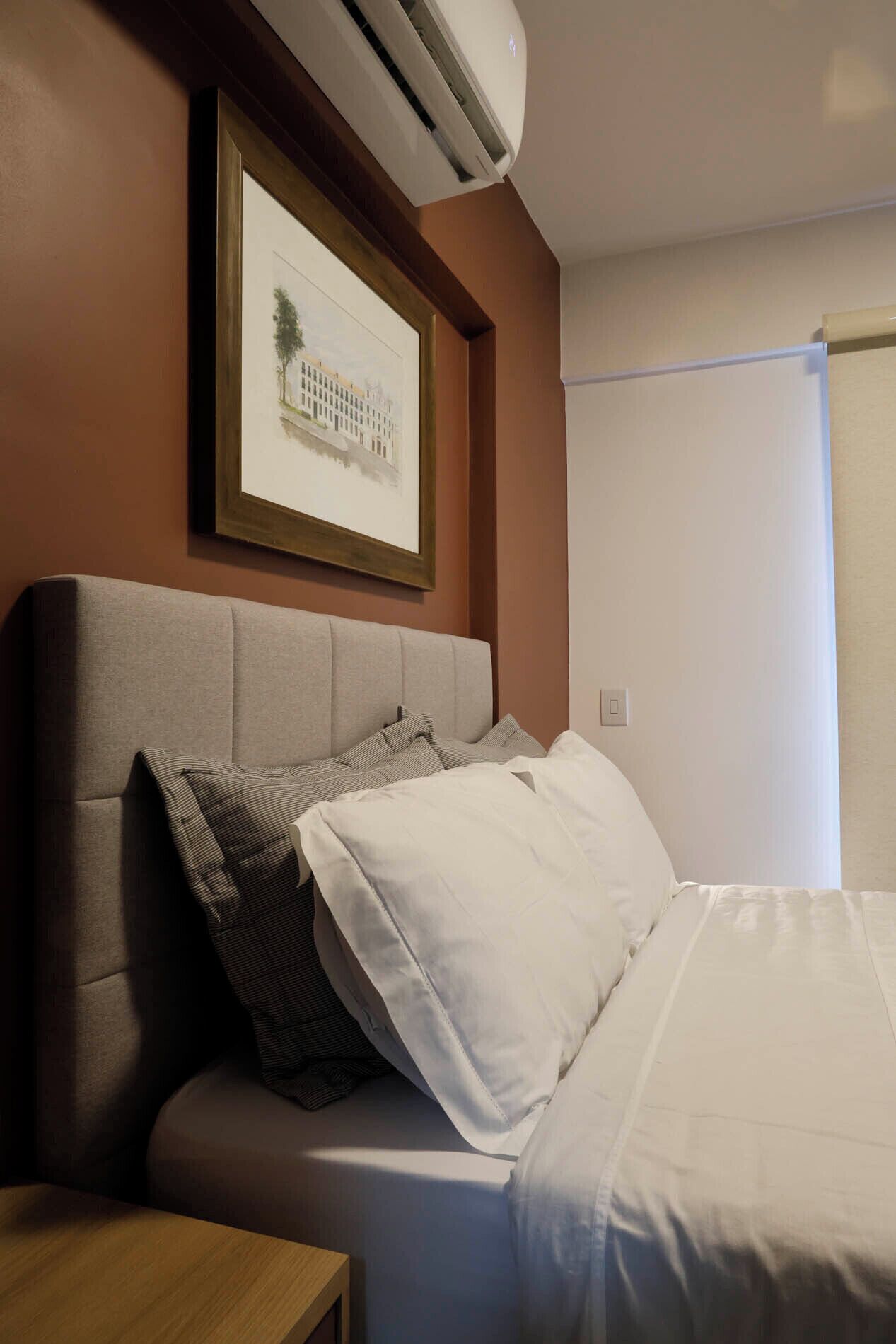 Una camera d'albergo con un letto, un comodino, un condizionatore d'aria e un quadro appeso al muro.