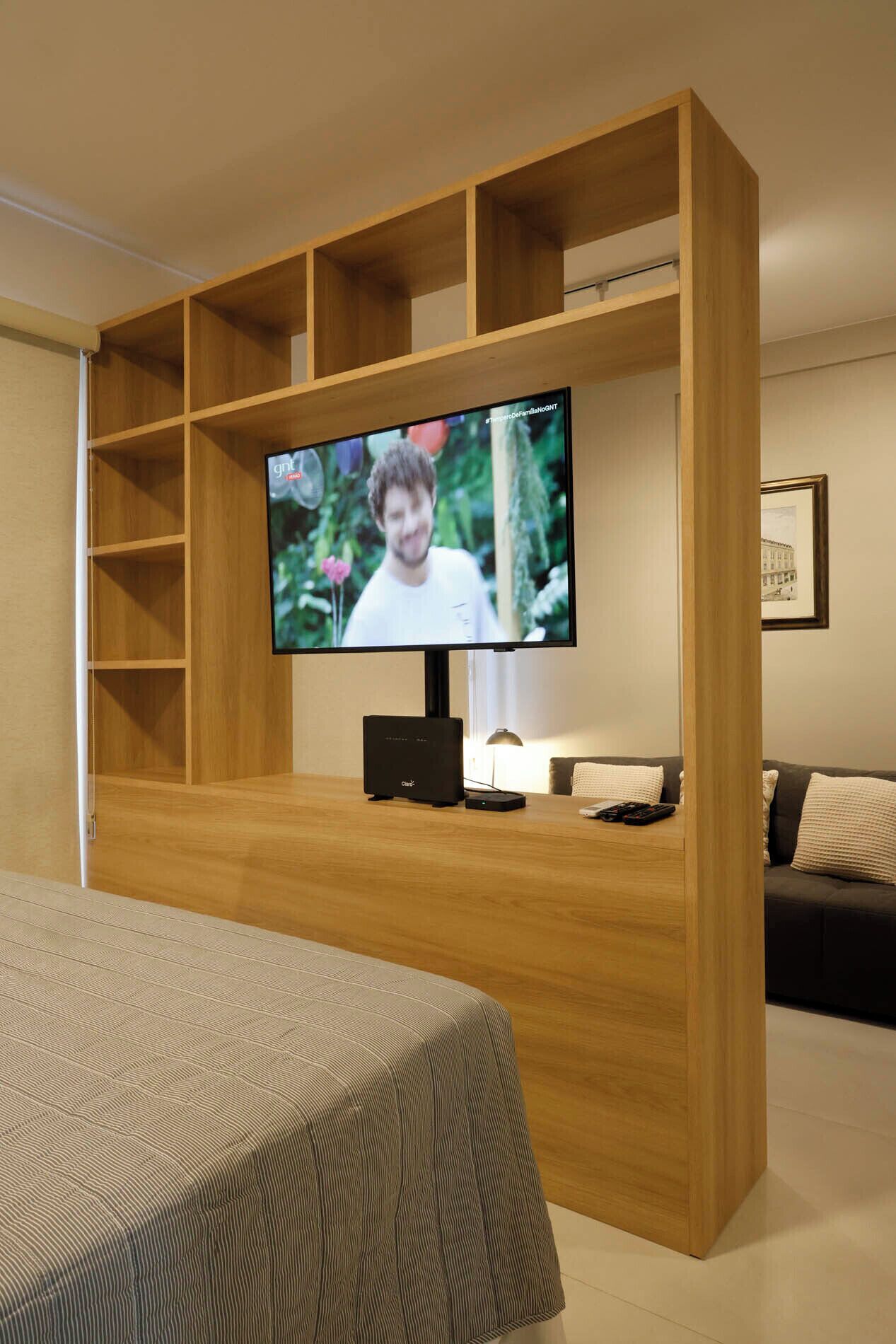 A modern living room with a wooden entertainment unit, a flat-screen TV, a sofa, and a bed.