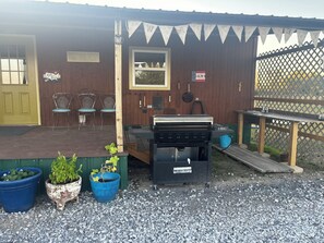A wooden porch with a grill, potted plants, and outdoor seating. - 3 Pines Private Lake Home (Warner)