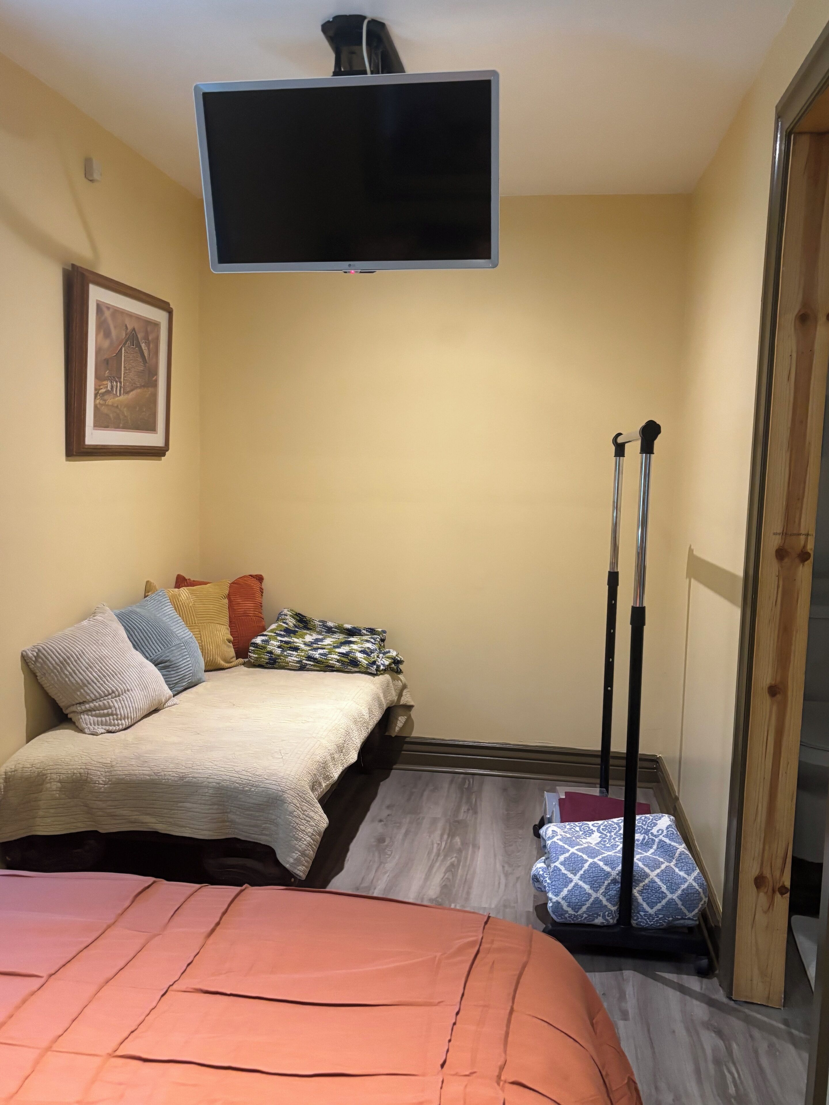 Une pièce avec un lit, un téléviseur fixé au mur, un tableau encadré et une porte en bois.