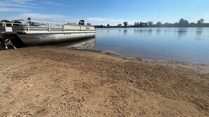 A boat docked at a sandy shore with calm water and a clear sky. - 3 Pines Private Lake Home (Warner)