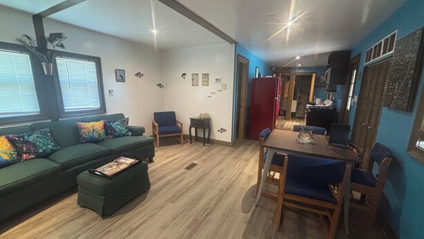 A living room with a green sofa, a wooden dining table with blue chairs, and a kitchen area in the background. - 3 Pines Private Lake Home (Warner)