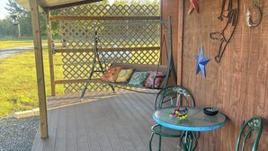 A covered patio with a wooden table and chairs, a swing, and decorative wall hangings. - 3 Pines Private Lake Home (Warner)