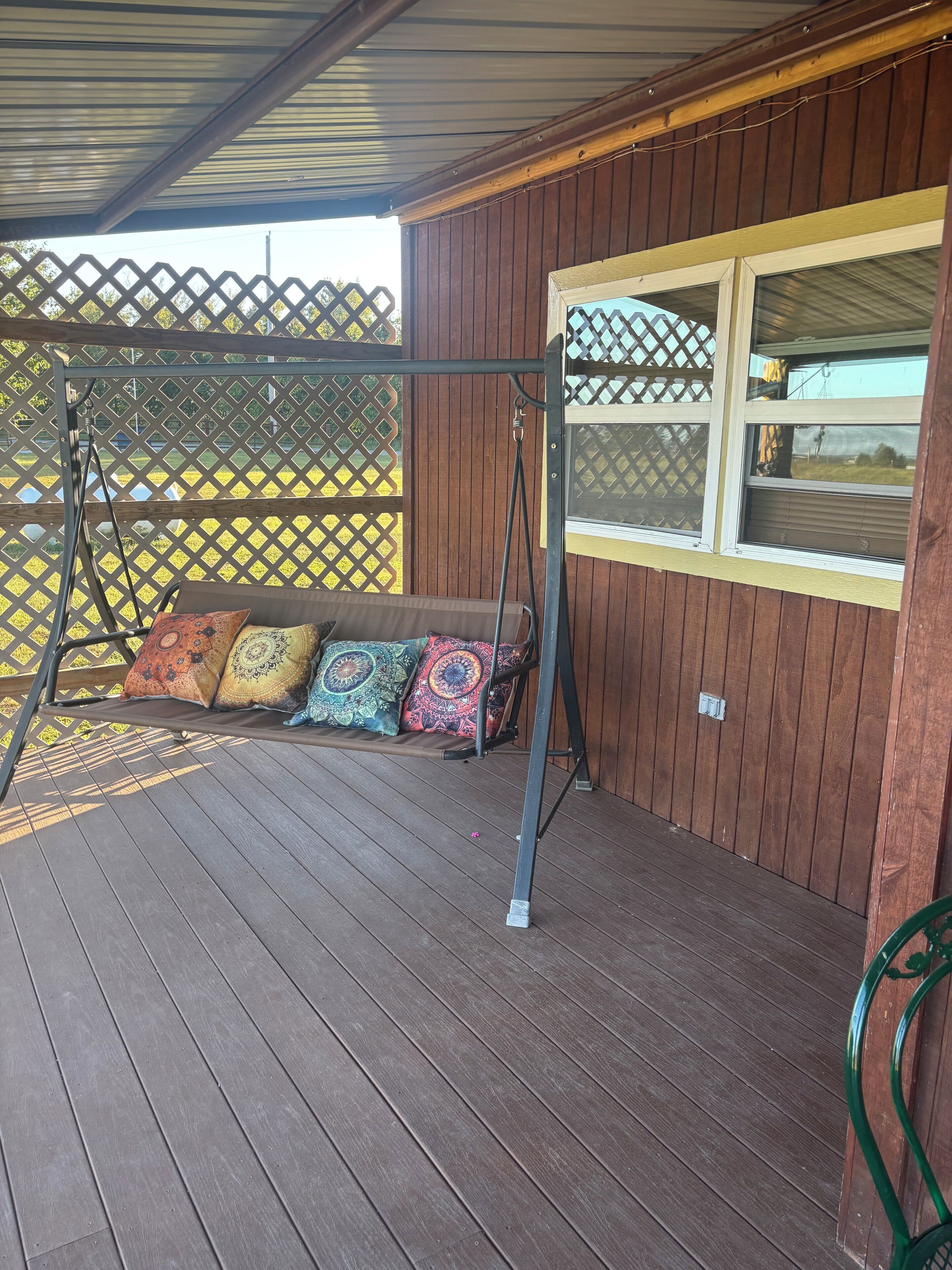 Une terrasse en bois avec une balançoire et un banc rembourré agrémenté de coussins colorés.