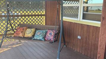 Une terrasse en bois avec une balançoire et un banc rembourré agrémenté de coussins colorés.