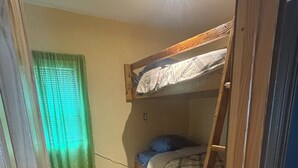 Una habitación con literas, una escalera, una ventana con cortinas verdes y una lámpara en el techo.
