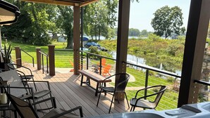 A hot tub on a wooden deck with outdoor furniture and a view of a lake and greenery.