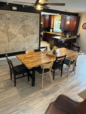 Un comedor con una mesa y sillas de madera, un mapa del mundo en la pared y una cocina al fondo.