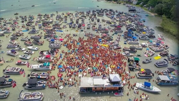 A large outdoor area with numerous boats docked in a circular formation, surrounded by a crowd of people.