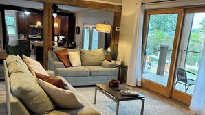 A spacious living room with a large sofa, a coffee table, and a view of the outdoor deck through large sliding glass doors.