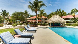 A resort pool area with lounge chairs, a thatched-roof structure, and palm trees. - 2BR Beachfront Villa w/ Pool, Sea View and Beach (Placencia)