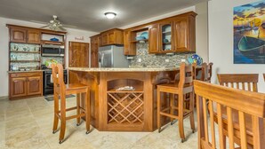 A kitchen with wooden cabinets, a central island with chairs, a ceiling fan, and a microwave. - 2BR Beachfront Villa w/ Pool, Sea View and Beach (Placencia)