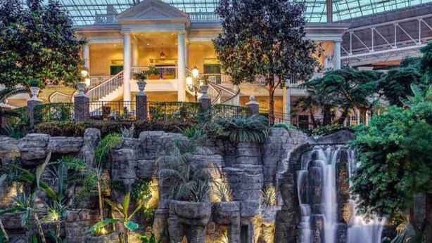 Eine Hotelhalle mit Wasserspiel, einer imposanten Treppe und üppiger Bepflanzung.