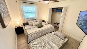 A bedroom with a bed, a ceiling fan, a window with curtains, and a TV mounted on the wall.