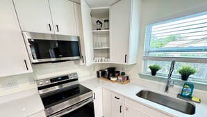 A modern kitchen with stainless steel appliances, white cabinetry, and a window with a view of greenery.