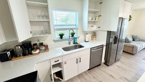 A modern kitchen with white cabinets, a stainless steel refrigerator, and a window with a view of greenery.