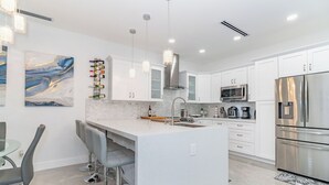 A modern kitchen with white cabinets, stainless steel appliances, and a bar area with stools.