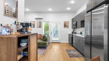 A modern kitchen with a built-in refrigerator, wooden cabinets, and a green sofa in the adjacent living area.