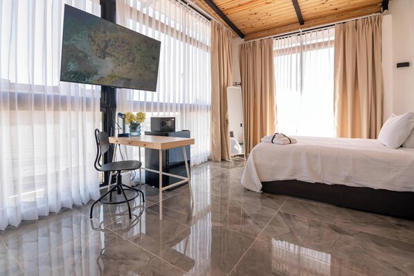 A modern bedroom with a bed, a desk with a chair, and a large window with sheer curtains.