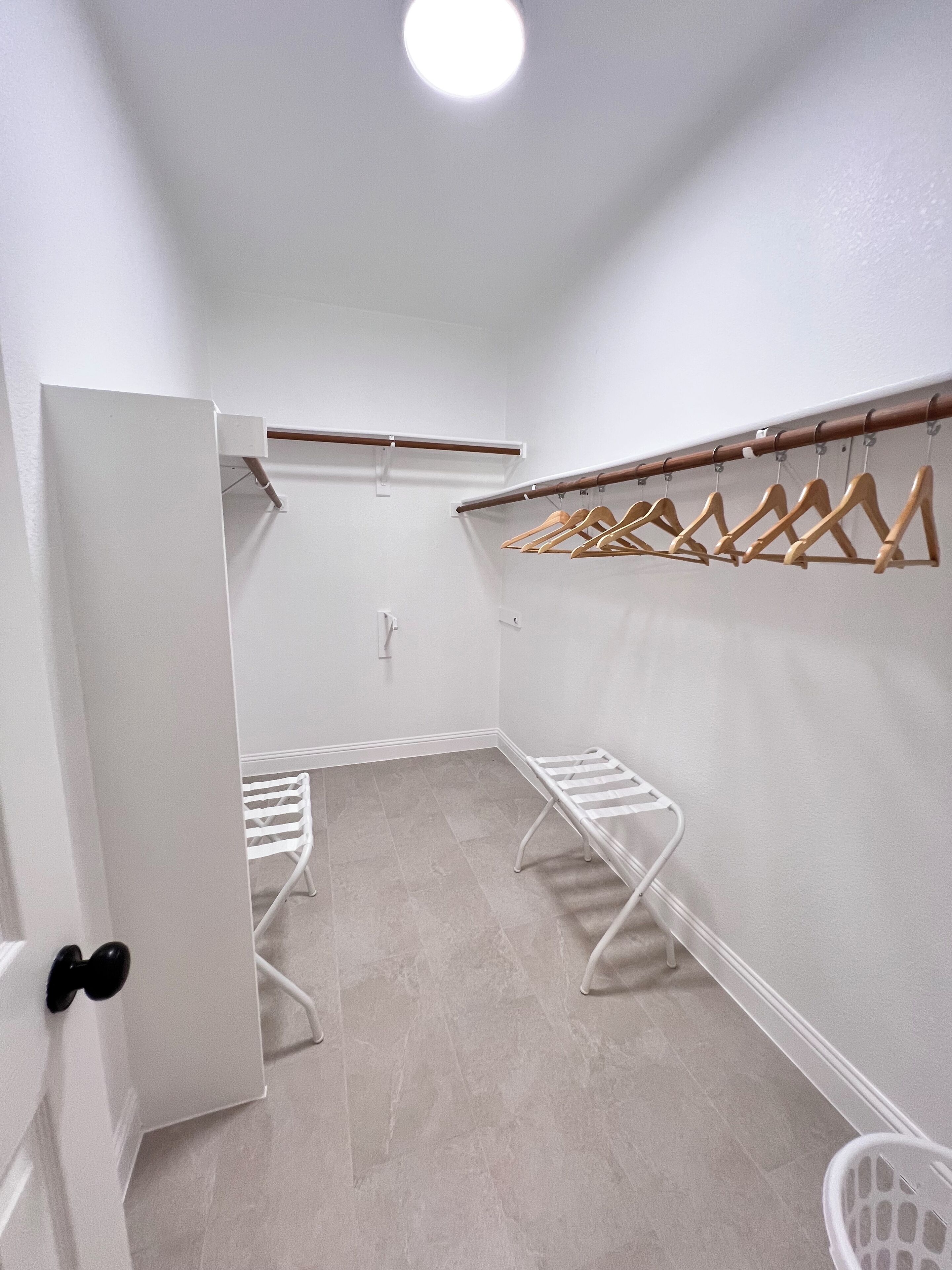 Ein begehbarer Kleiderschrank mit Holzkleiderbügeln und einem weißen Wäscheständer.