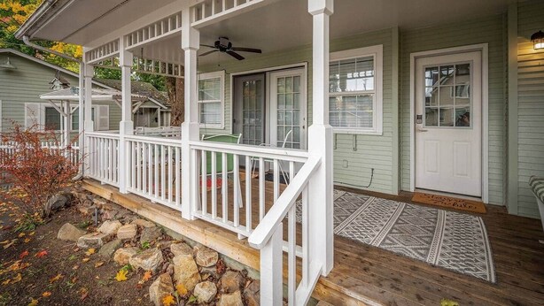 A covered porch with a white railing, a ceiling fan, and a door with a small porch rug. - Charming Downtown Home, Walk to CDA Shops&Eateries (Coeur d'Alene)