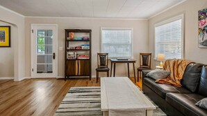 A living room with a wooden floor, a bookshelf, a dining table with chairs, a sofa, and a window with blinds. - Charming Downtown Home, Walk to CDA Shops&Eateries (Coeur d'Alene)