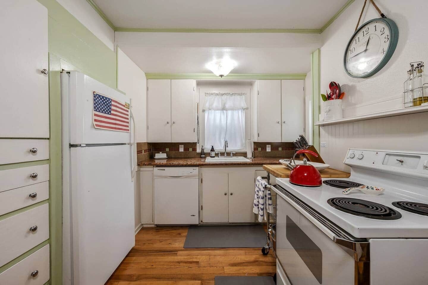A compact kitchen with white cabinets, a stove, a sink, and a clock on the wall.