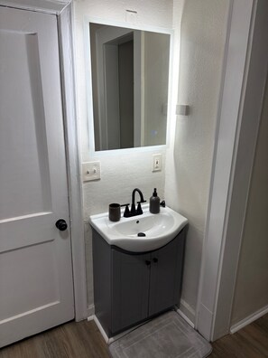 Un baño con un lavamanos blanco, un espejo y una puerta.