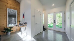 A modern interior with wooden walls, a desk with books, a potted plant, and a view of a green outdoor area through a glass door. - Spa & forest in St-Donat/Tremblant - Nature and relaxation getaway (Notre-Dame-de-la-Merci)