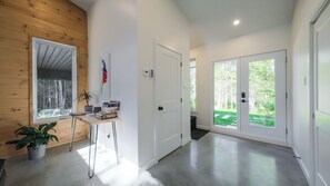 Interior moderno com paredes de madeira, uma escrivaninha com livros, uma planta em vaso e vista para área verde através de uma porta de vidro.