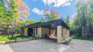 A modern house with a covered porch, surrounded by trees and a gravel driveway. - Spa & forest in St-Donat/Tremblant - Nature and relaxation getaway (Notre-Dame-de-la-Merci)