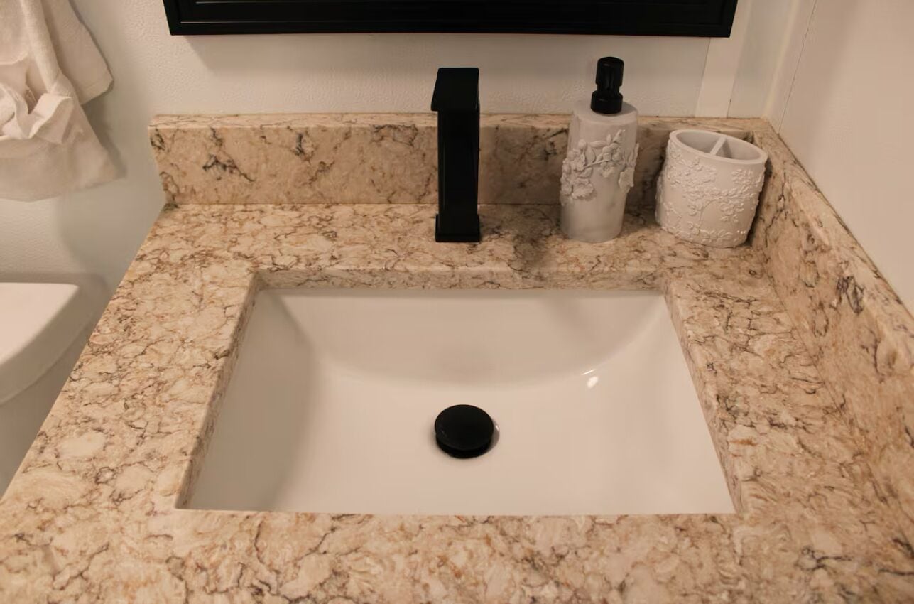 Un baño con un lavamanos de mármol, un grifo negro y dos jarrones decorativos.